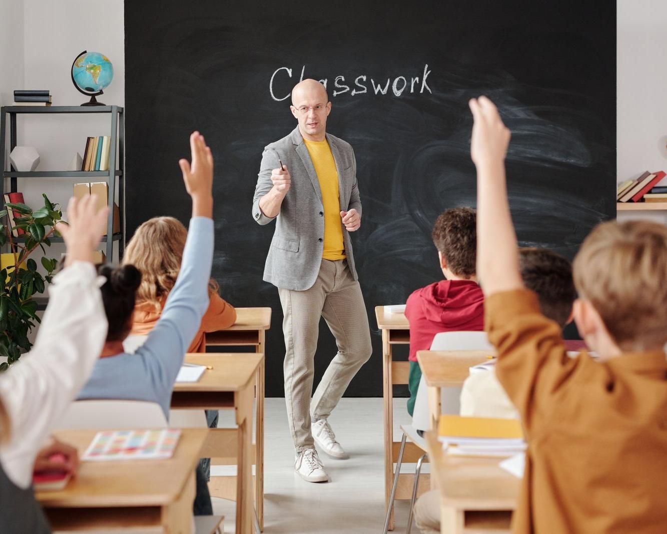 Teacher in front of a class of students raising their hands